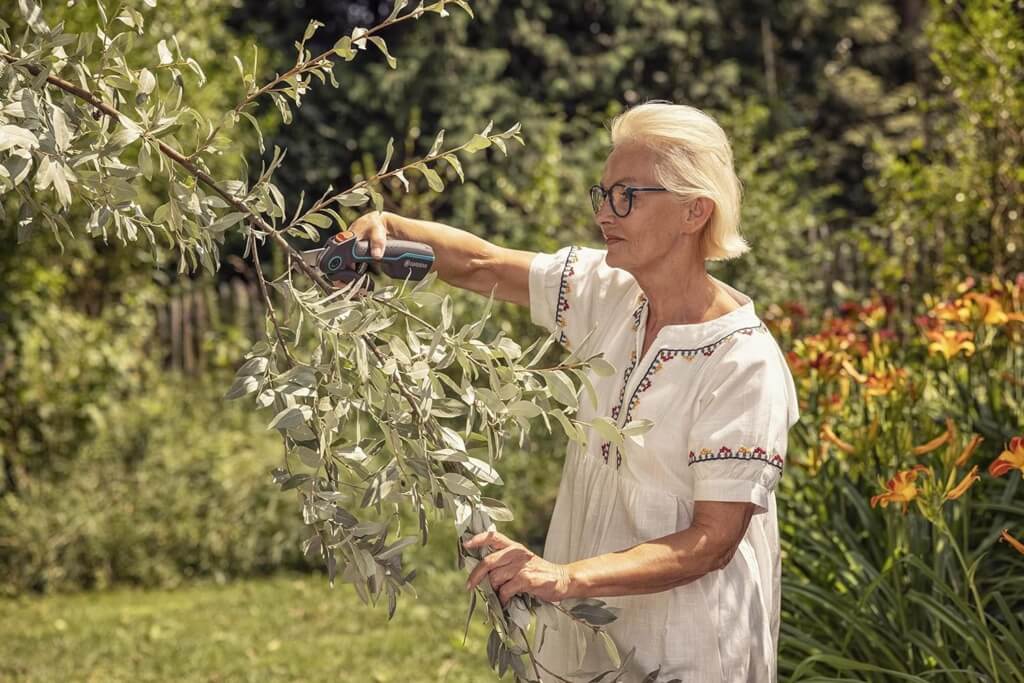 Frau schneidet mit einer elektrischen Schere Pflanzen in einem blühenden Garten.