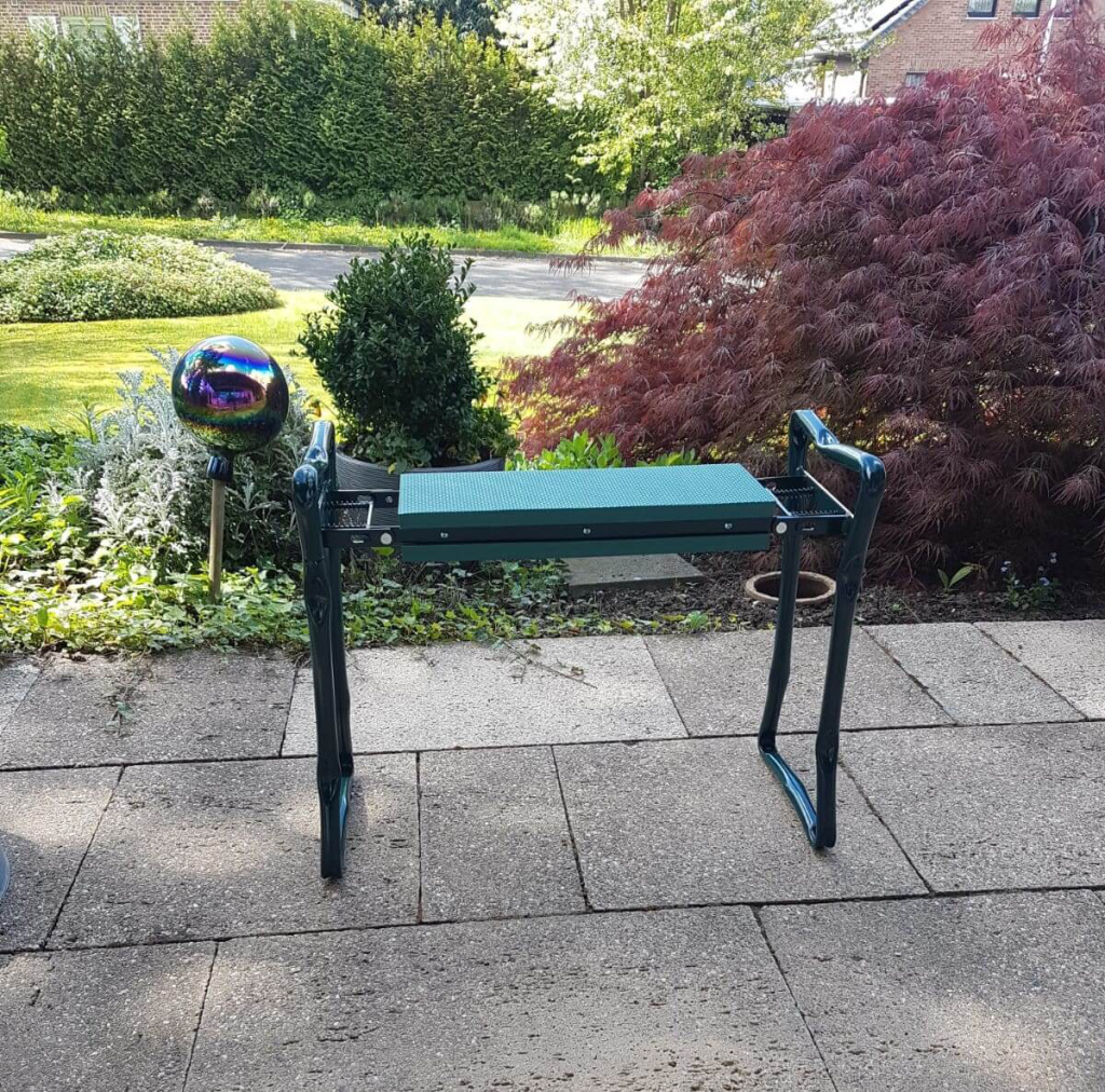 Gartenarbeitsplatz mit grüner Oberfläche, dekorative Kugel im Hintergrund, blühende Pflanzen.